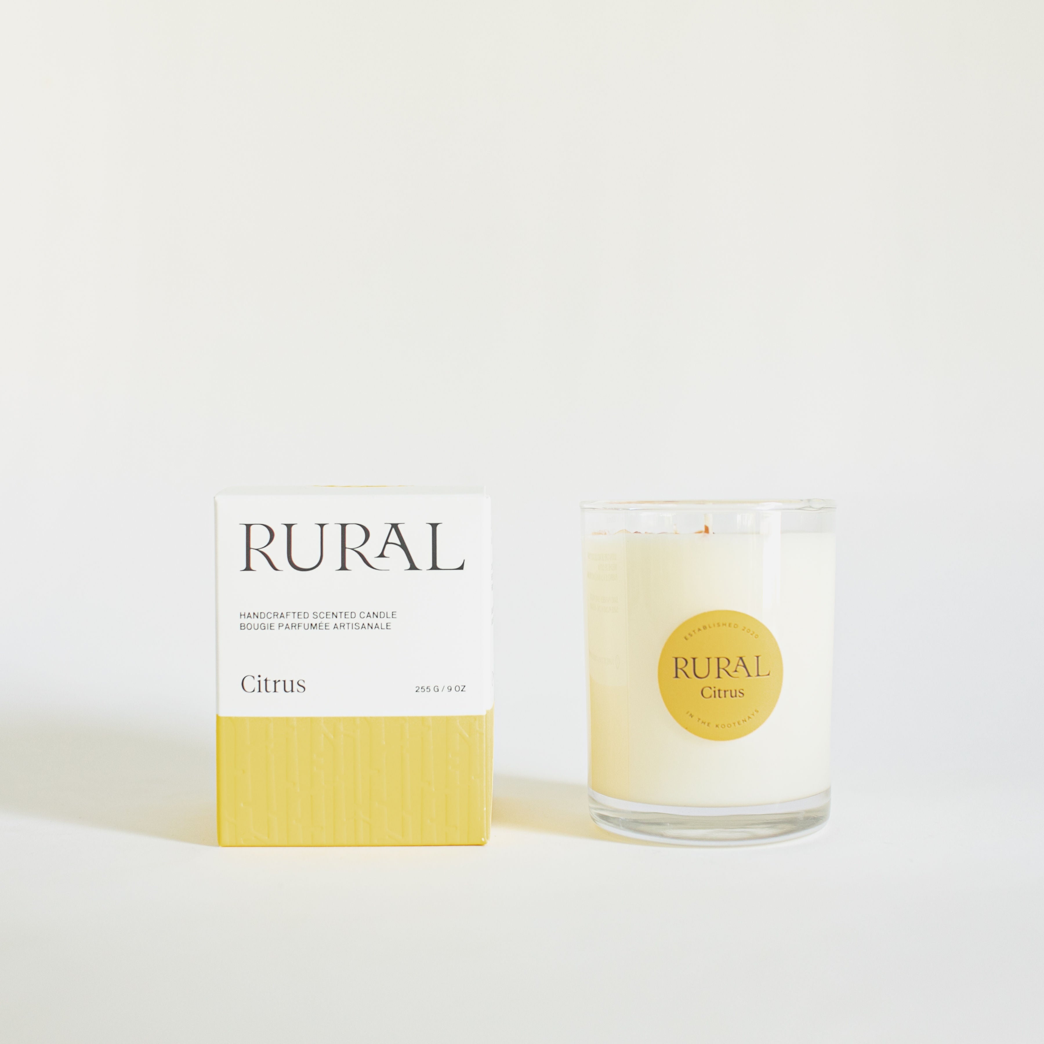 Product photo of a Citrus candle in a clear glass container with a yellow round RURAL Candles label on it, alongside its matching yellow and white RURAL Candles gift box.