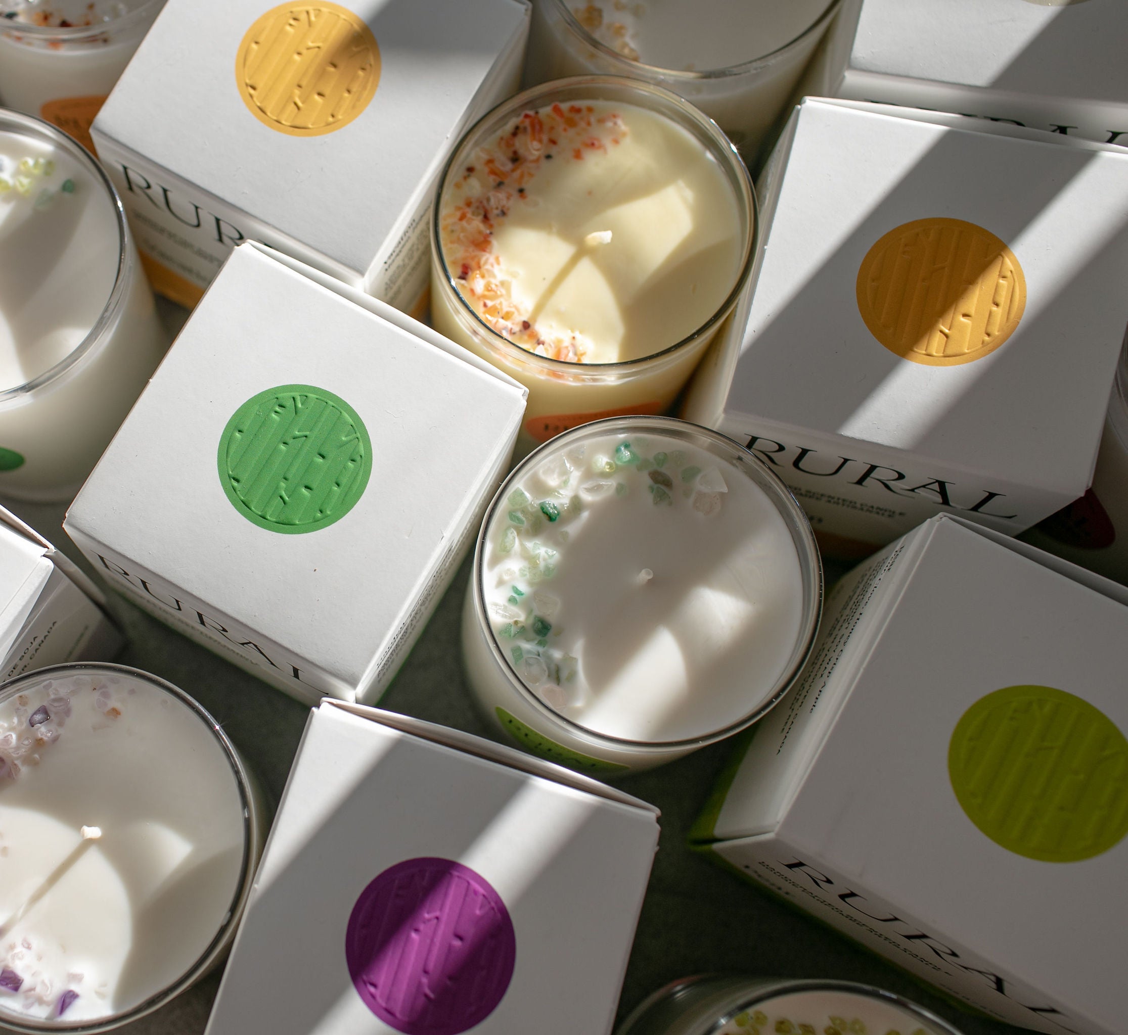 Photo of the top view of a group of candles tastefully decorated with multicolored gemstones arranged in the shape of a half-moon, alongside colorful, embossed candle boxes that match the gemstones.