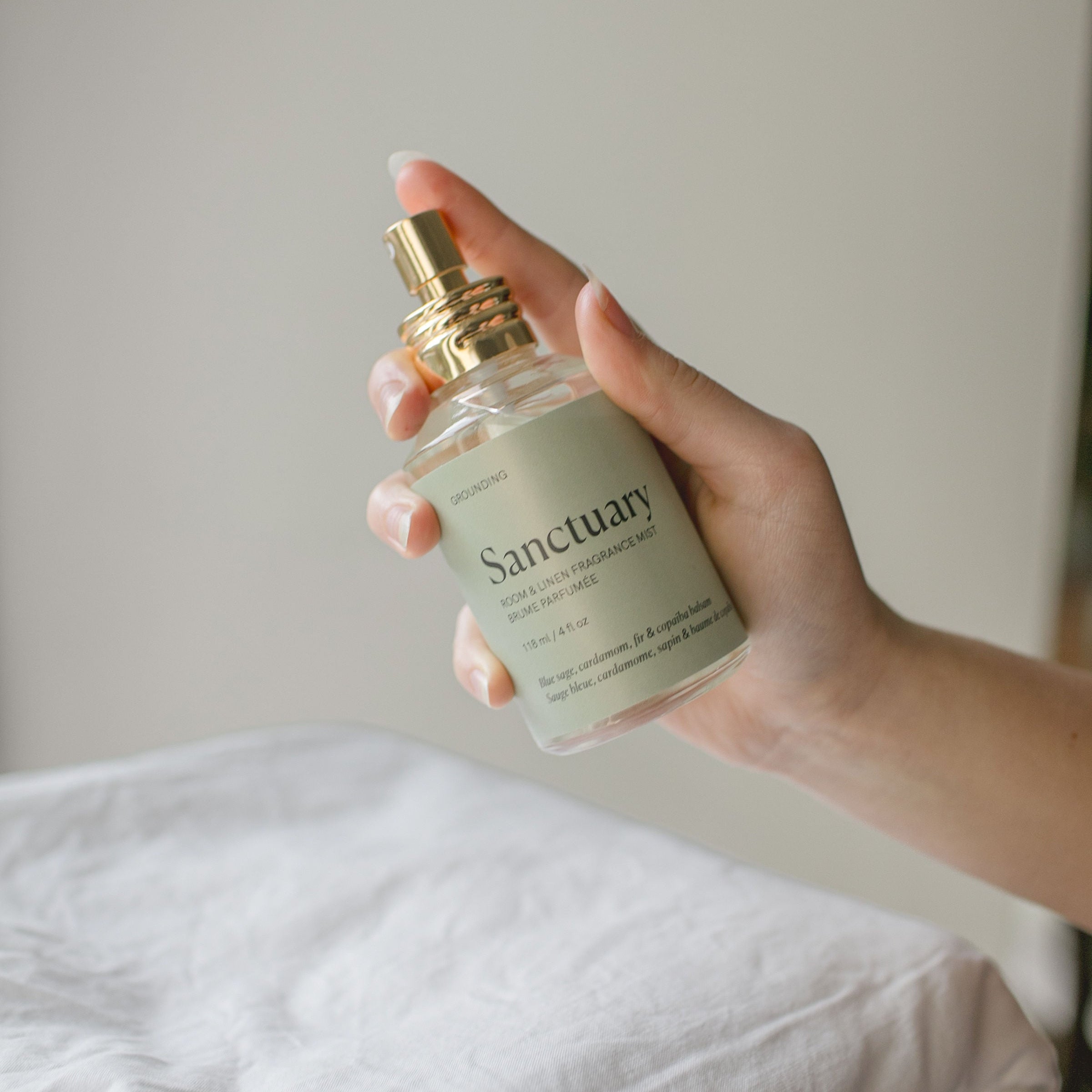 Hand holding a bottle labeled 'Sanctuary' against a neutral background