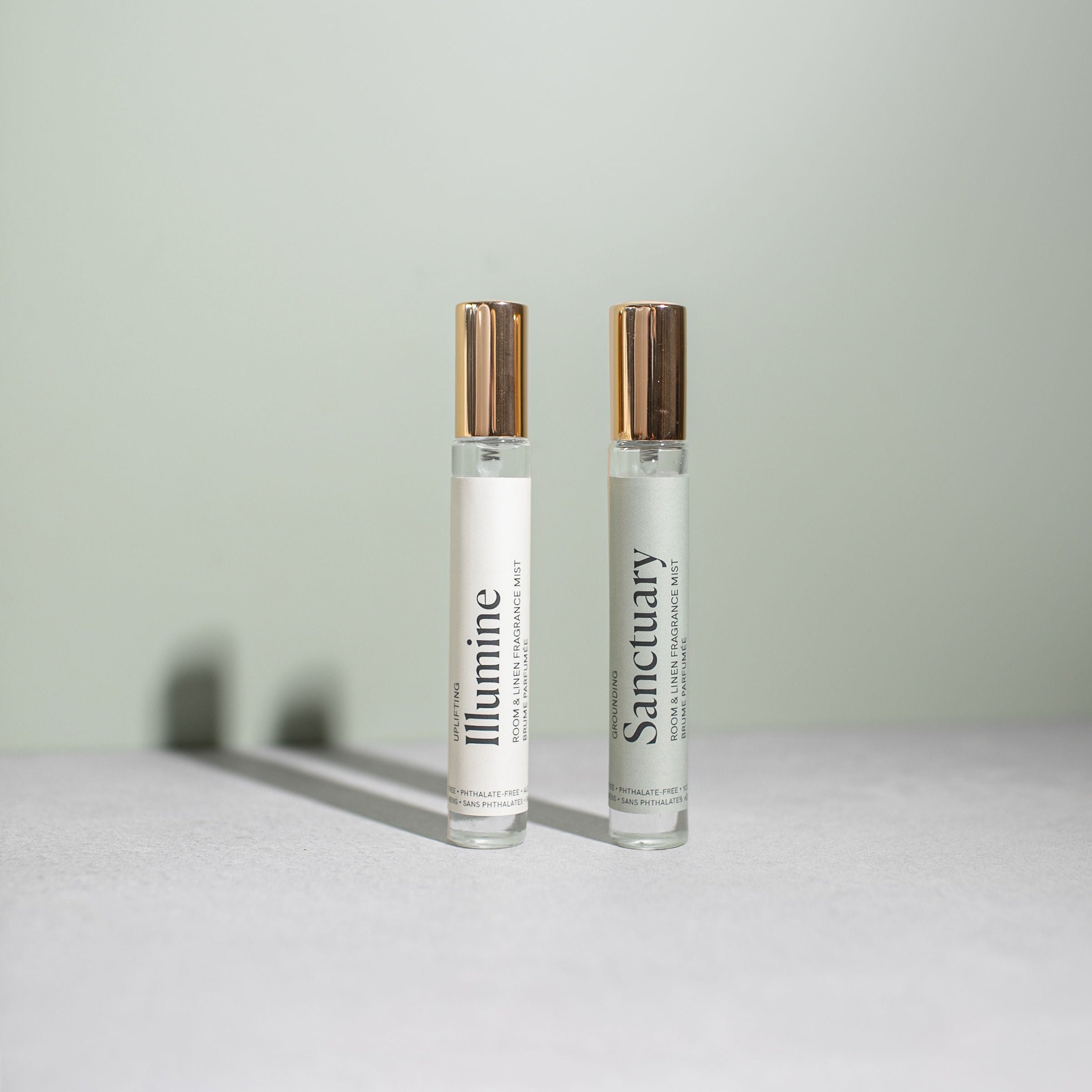Two small glass bottles labeled 'Illumine' and 'Sanctuary' on a light surface with a light green background.