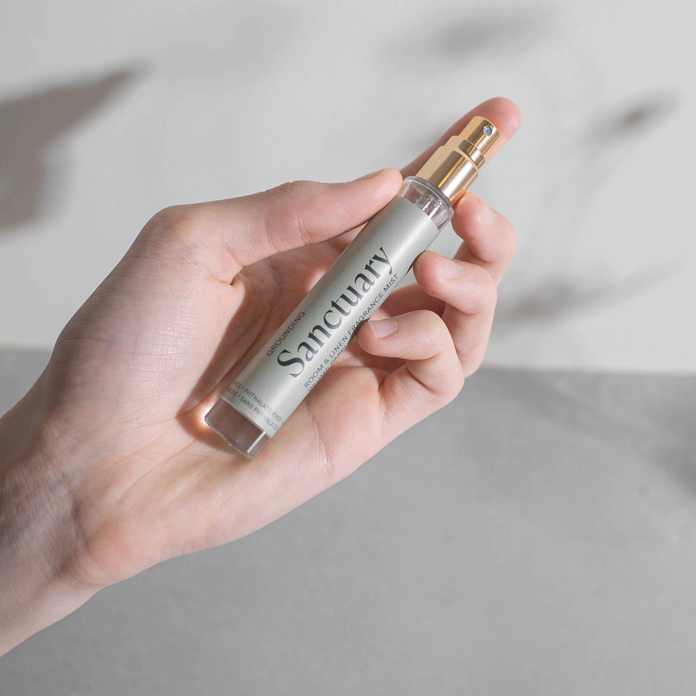 Hand holding a small glass spray bottle labelled 'Sanctuary' against a neutral background