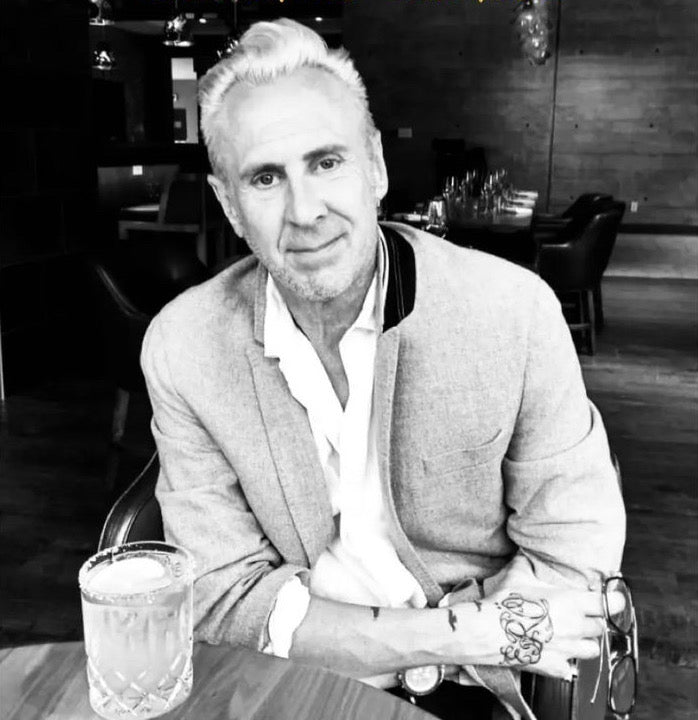 Black and white photo of Duane, the founder and artist of RURAL Candles, who passed away from cancer. He's wearing a wool blazer and white dress shirt, and sitting in a cocktail lounge.