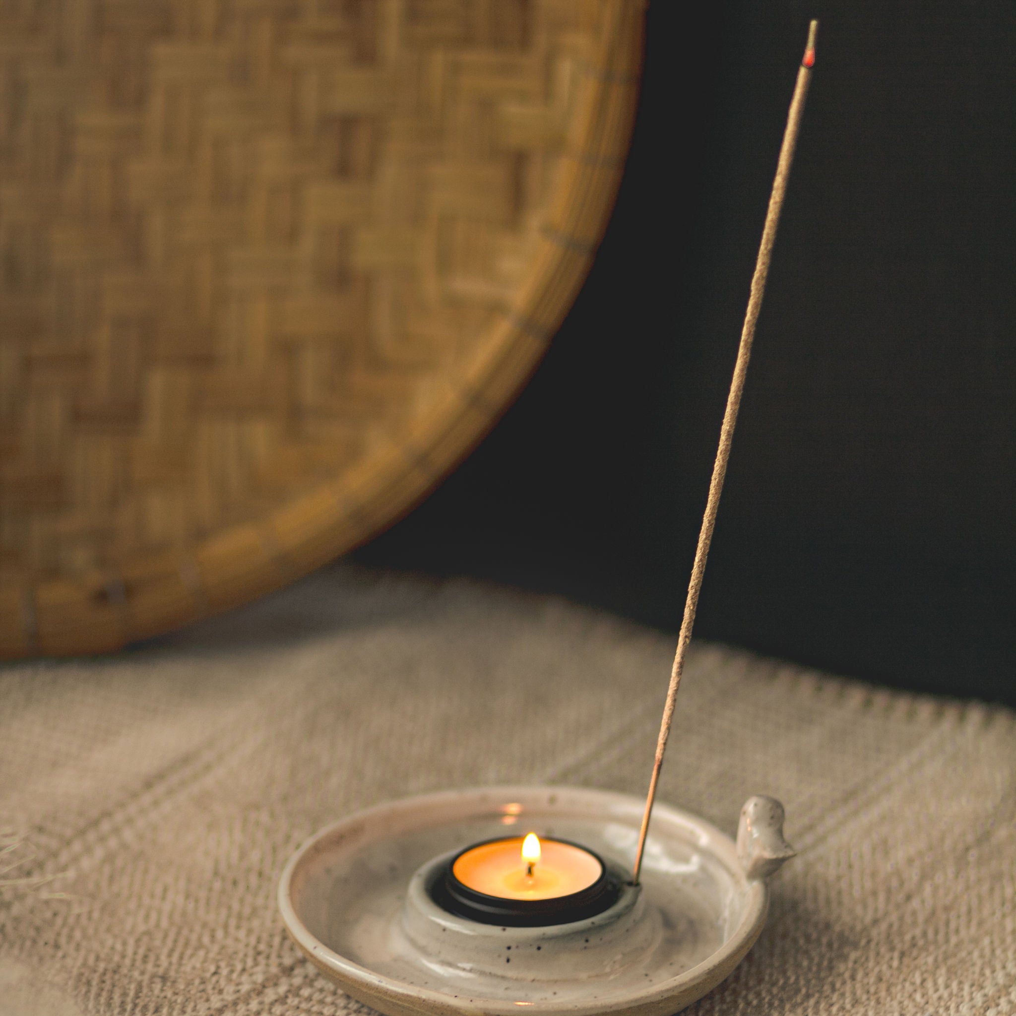 Incense stick burning in a small ceramic holder with a woven mat background