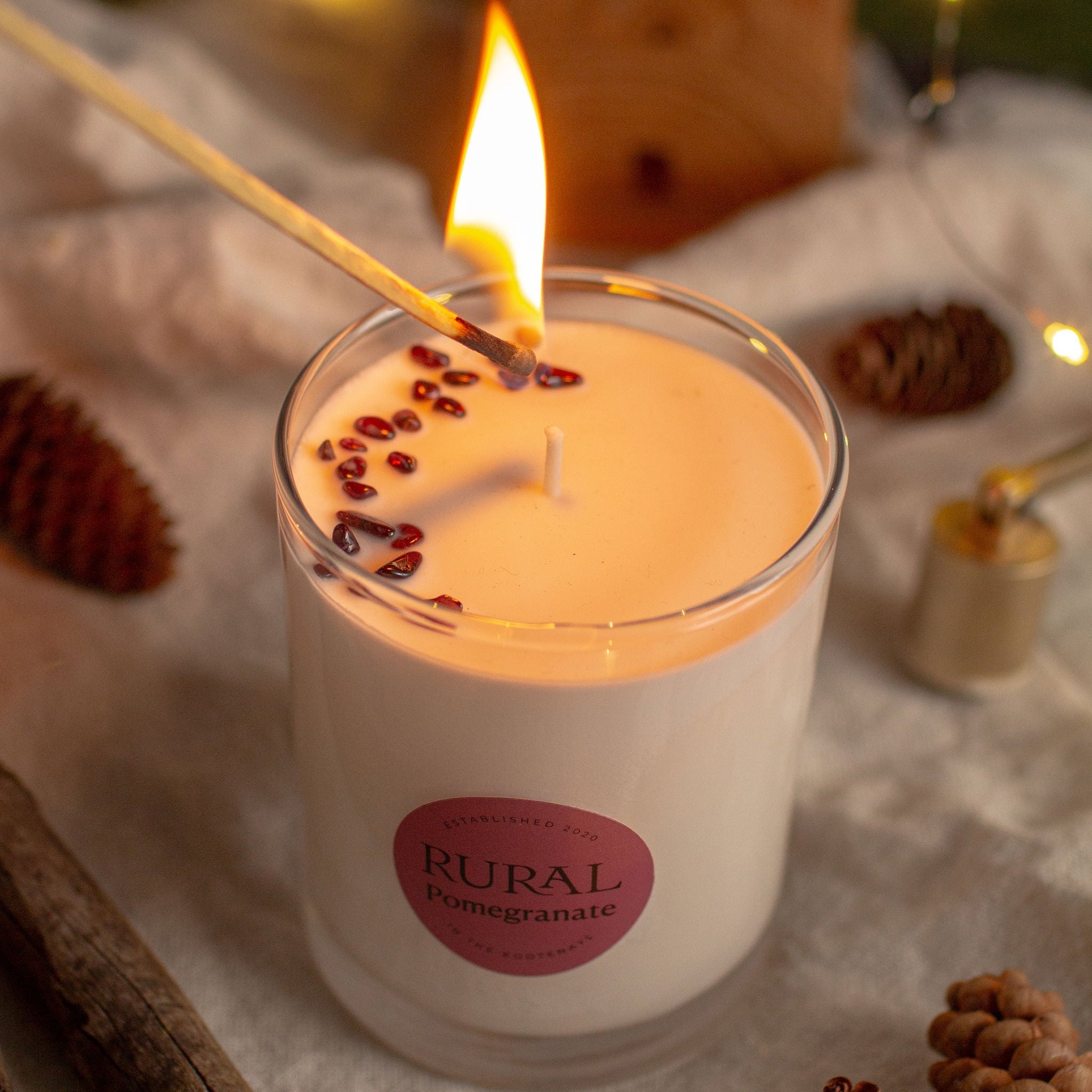 Top view of the RURAL Candles pomegranate candle just about to be lit with a match. We can see the garnet gemstones on the candle. The setting is rustic cottage cozy.