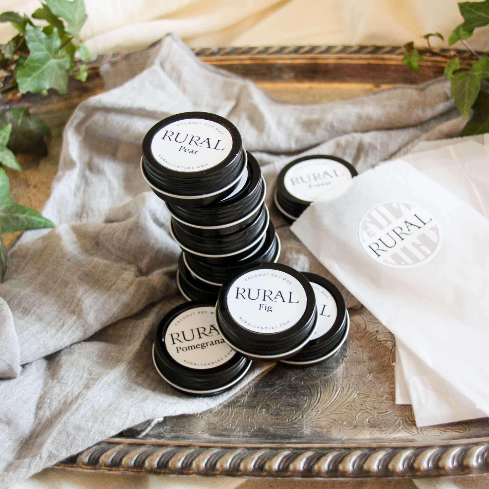 This is a photo of a little stacked grouping of 9 tealight candles. Each candle is in an elegant black tin with a white and black circular label for each scent, such as Pear, Fig, and Pomegranate.