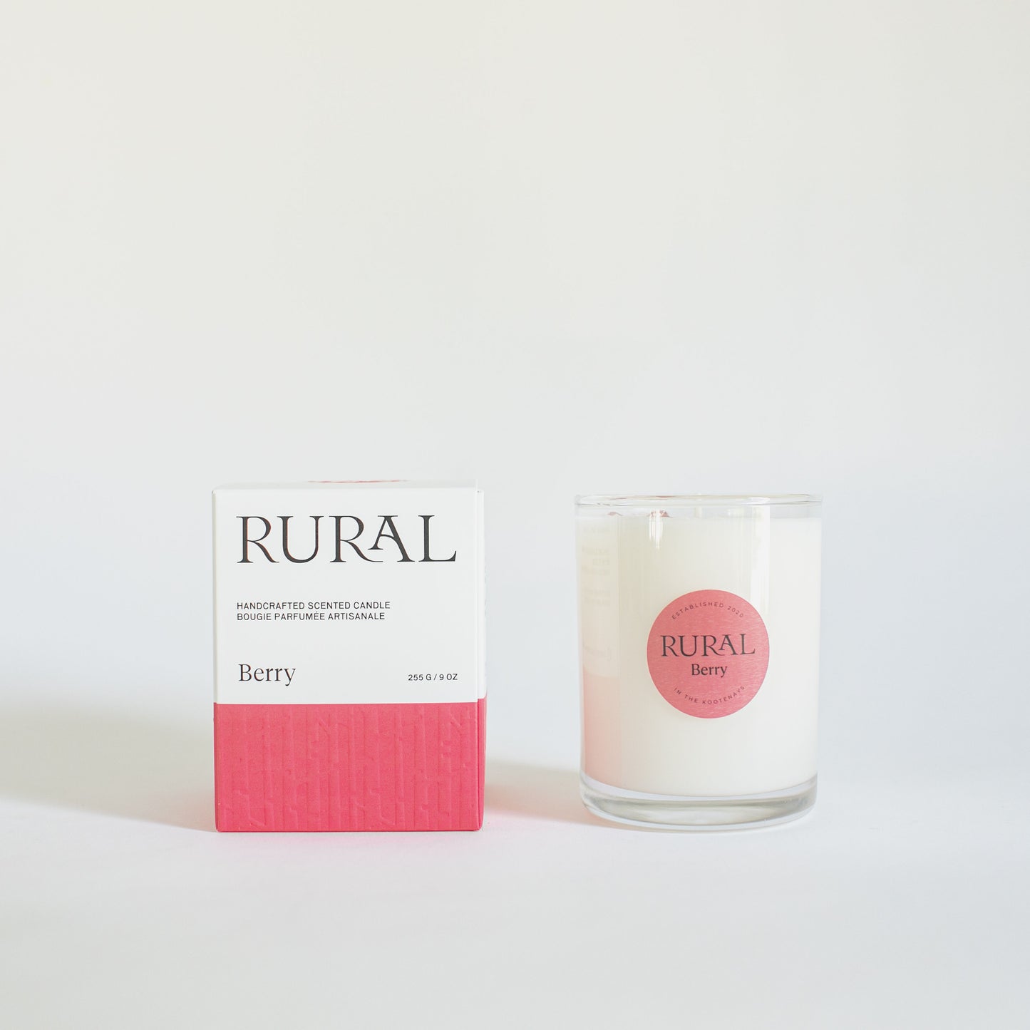 Product photo of a white candle in clear glass container with a pink round RURAL Candles label on, indicating its Berry scent. Alongside is a matching pink and white Berry Candle gift box with the RURAL Candles logo on it.