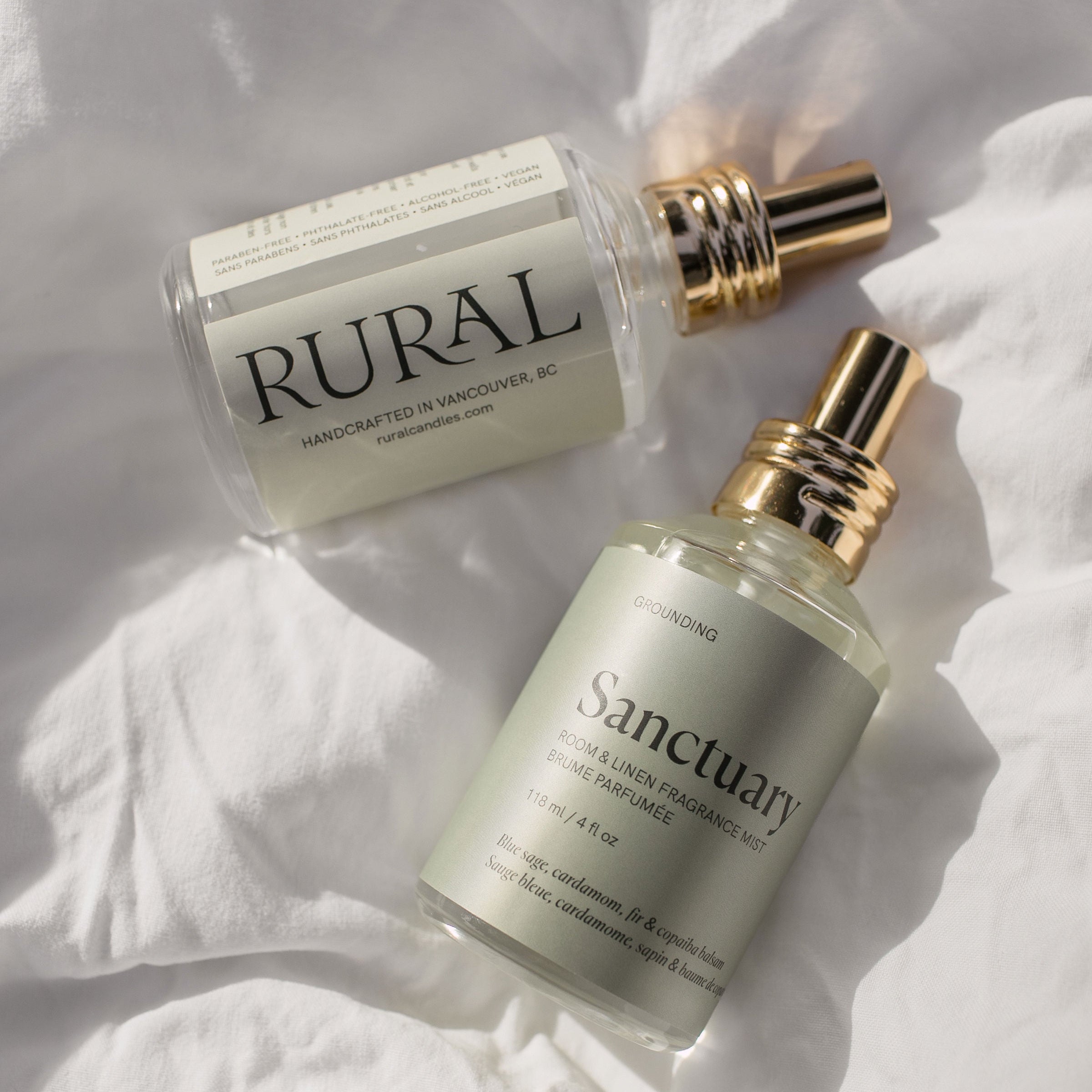 Two glass bottles of room & linen fragrance mist on a white fabric background