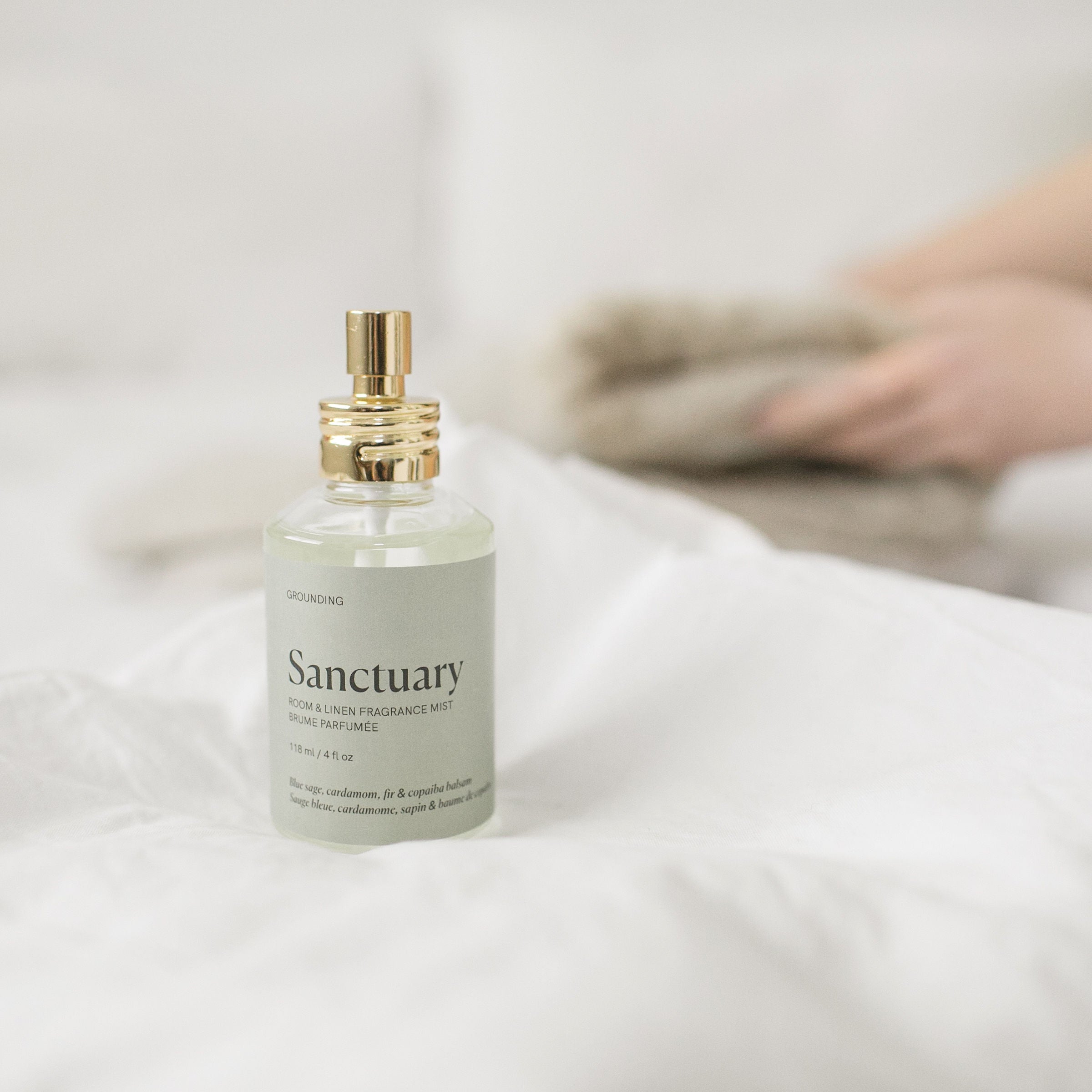 Bottle of 'Sanctuary' room spray on a white surface with a blurred background