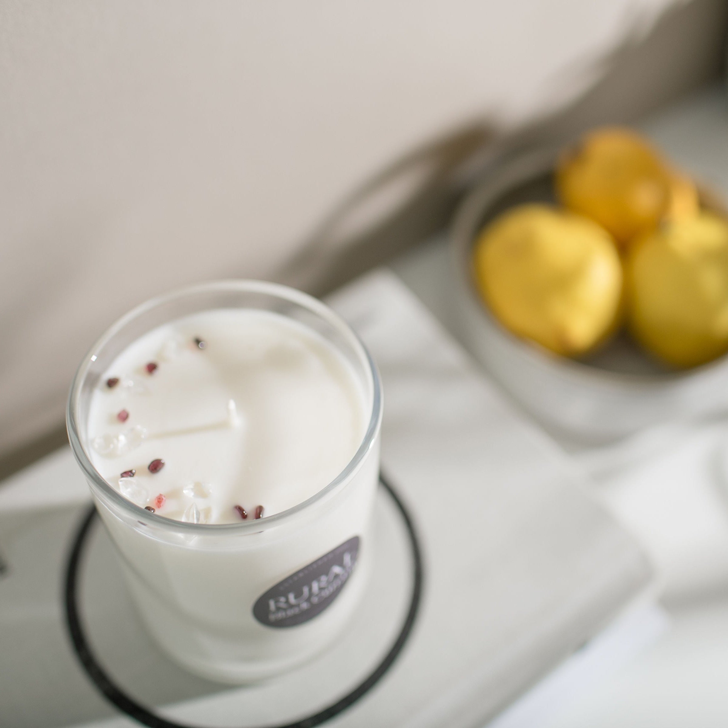 white candle with garnet and clear quartz gemstones sprinkled on top, on a white background with lemons