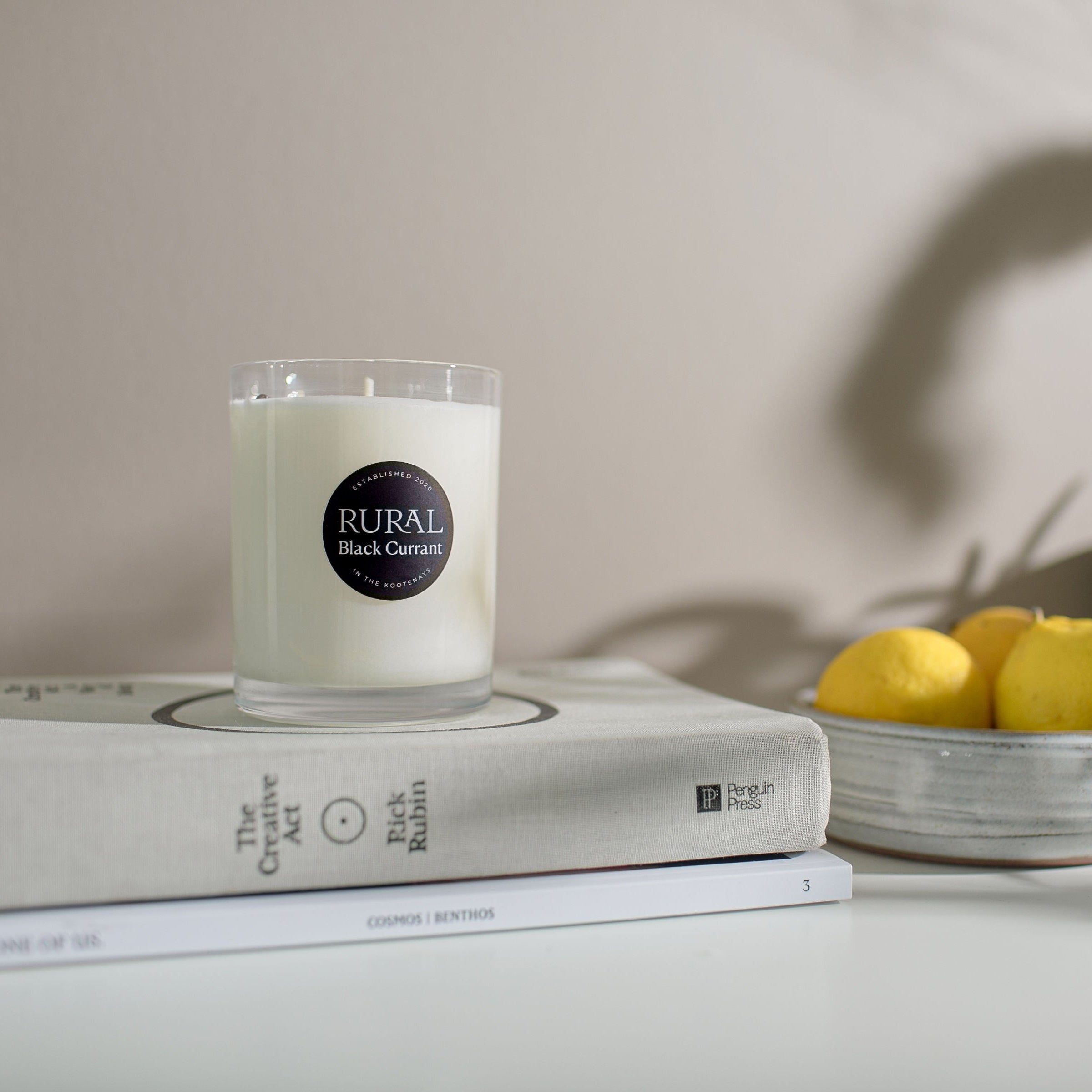 Candle on books with a bowl of lemons and a plant in the background