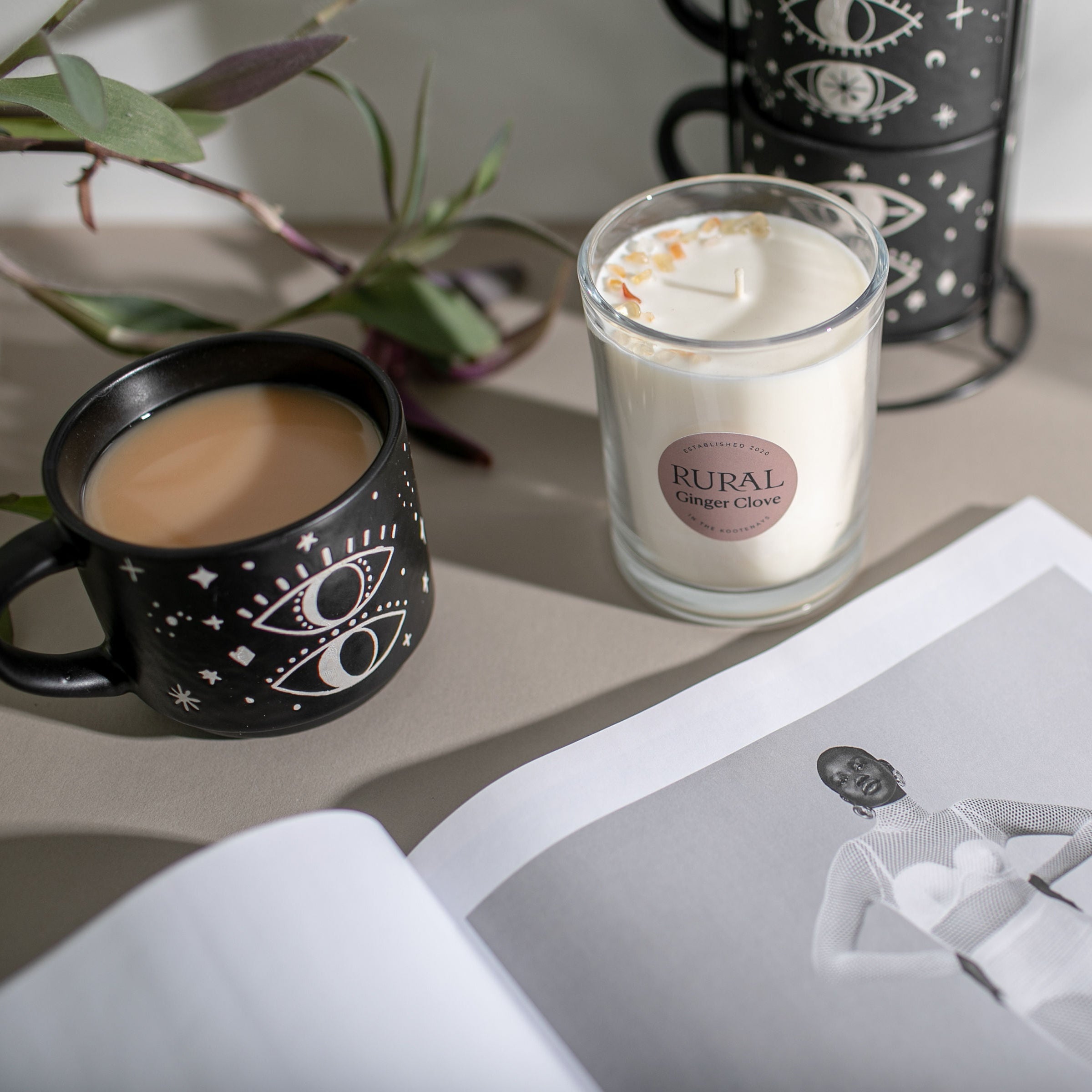 Rural Candle labelled Ginger Clove next to a mug with a drink on a surface with a plant in the background