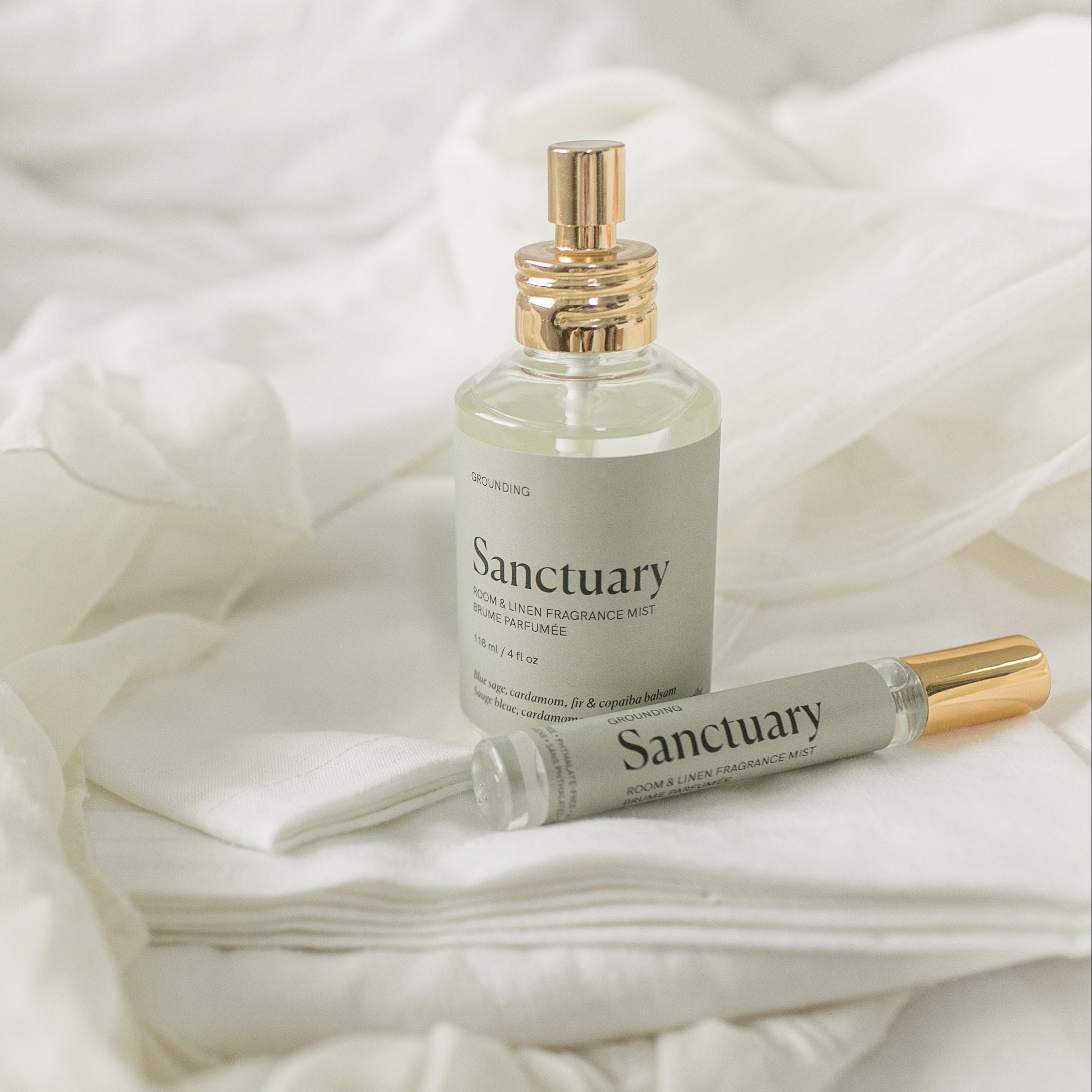 Two bottles of Sanctuary scented room mists on a white fabric background