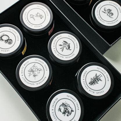Set of small containers with black lids and white labels arranged in a box on a light background