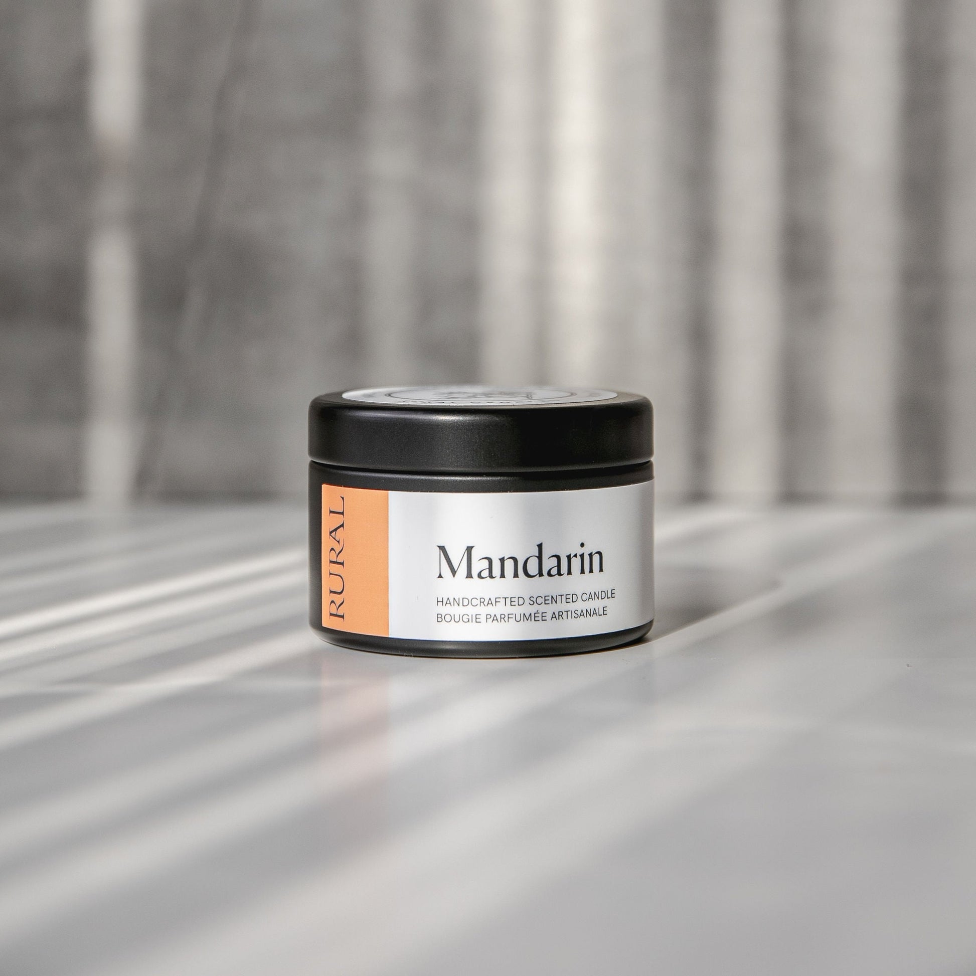 Mandarin scented black candle tin with orange and white label on a reflective surface with a neutral background.