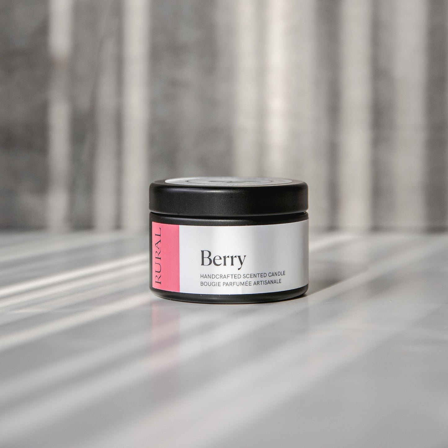 Berry scented black candle tin with pink and white label on a reflective surface with a neutral background.