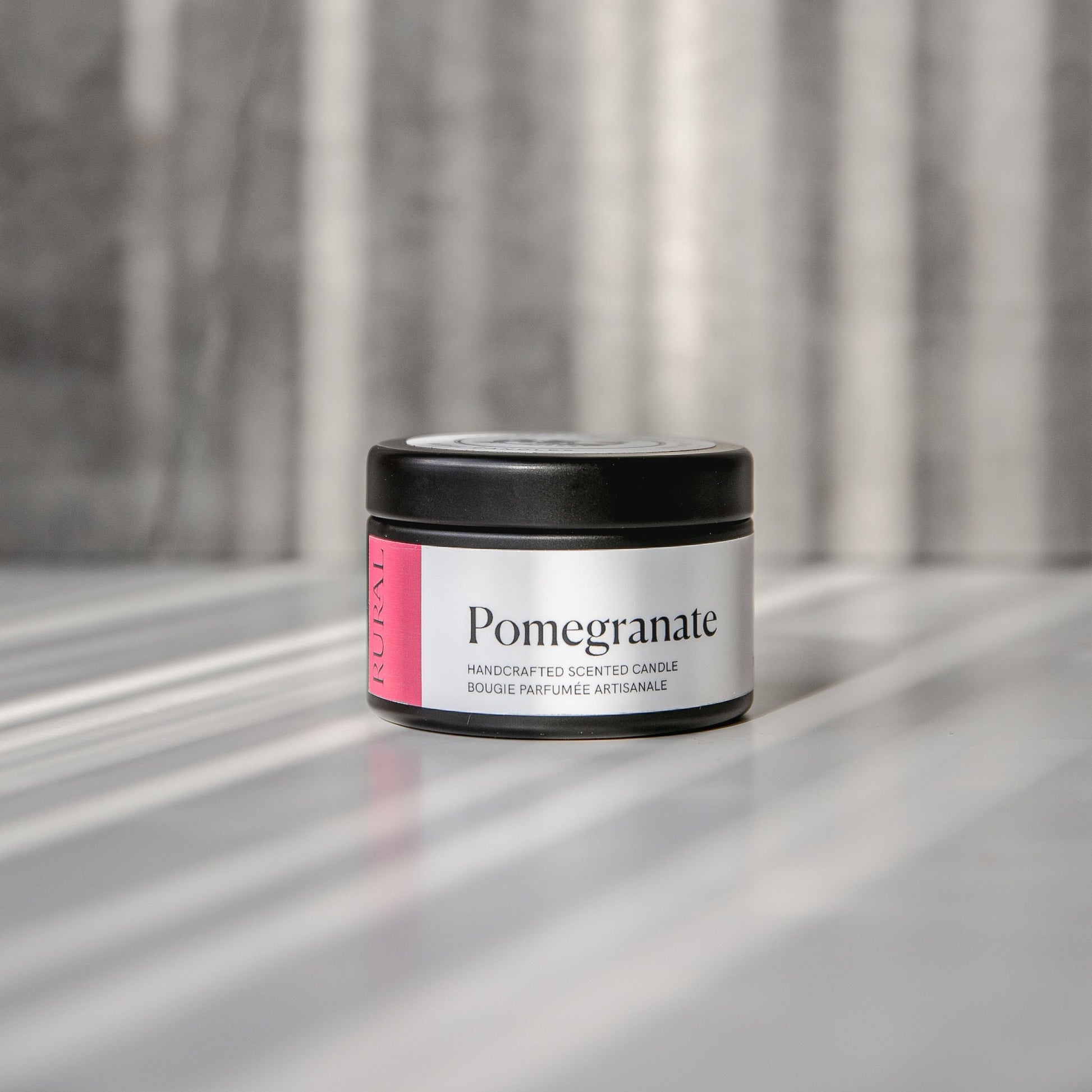 Pomegranate scented black candle tin with red and white label on a reflective surface with a neutral background.