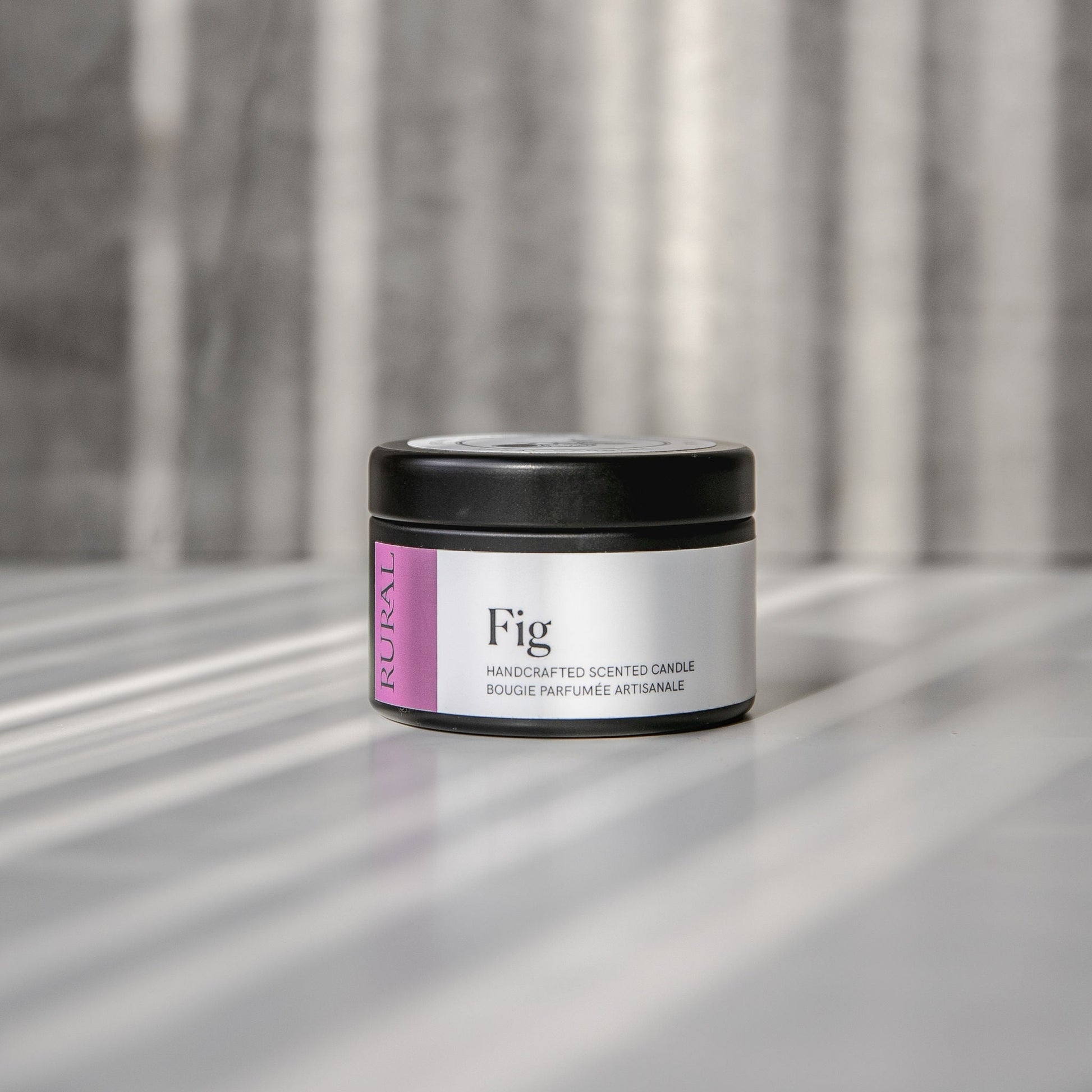 Fig scented black candle tin with purple and white label on a reflective surface with a neutral background.