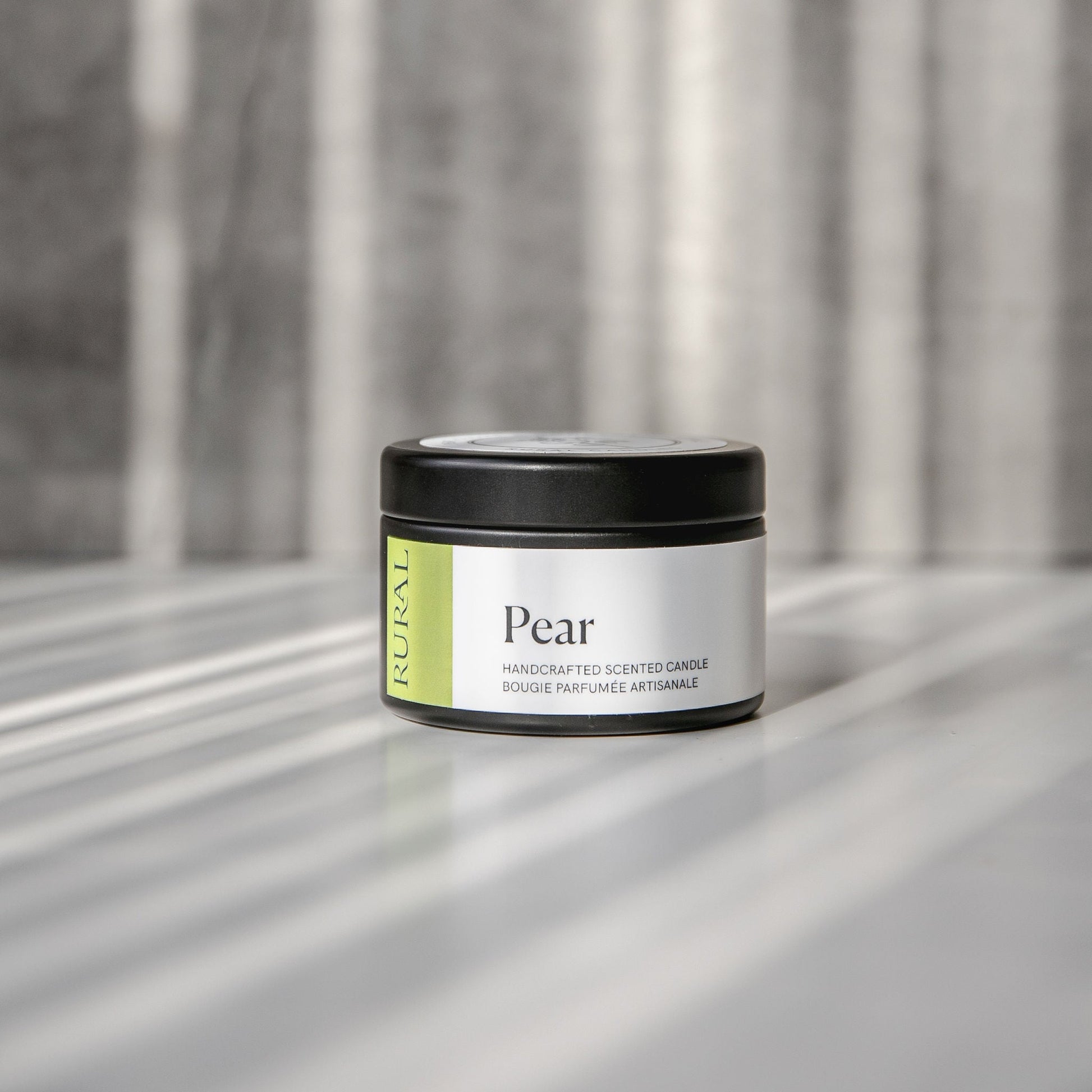 Pear scented black candle tin with green and white label on a reflective surface with a neutral background.