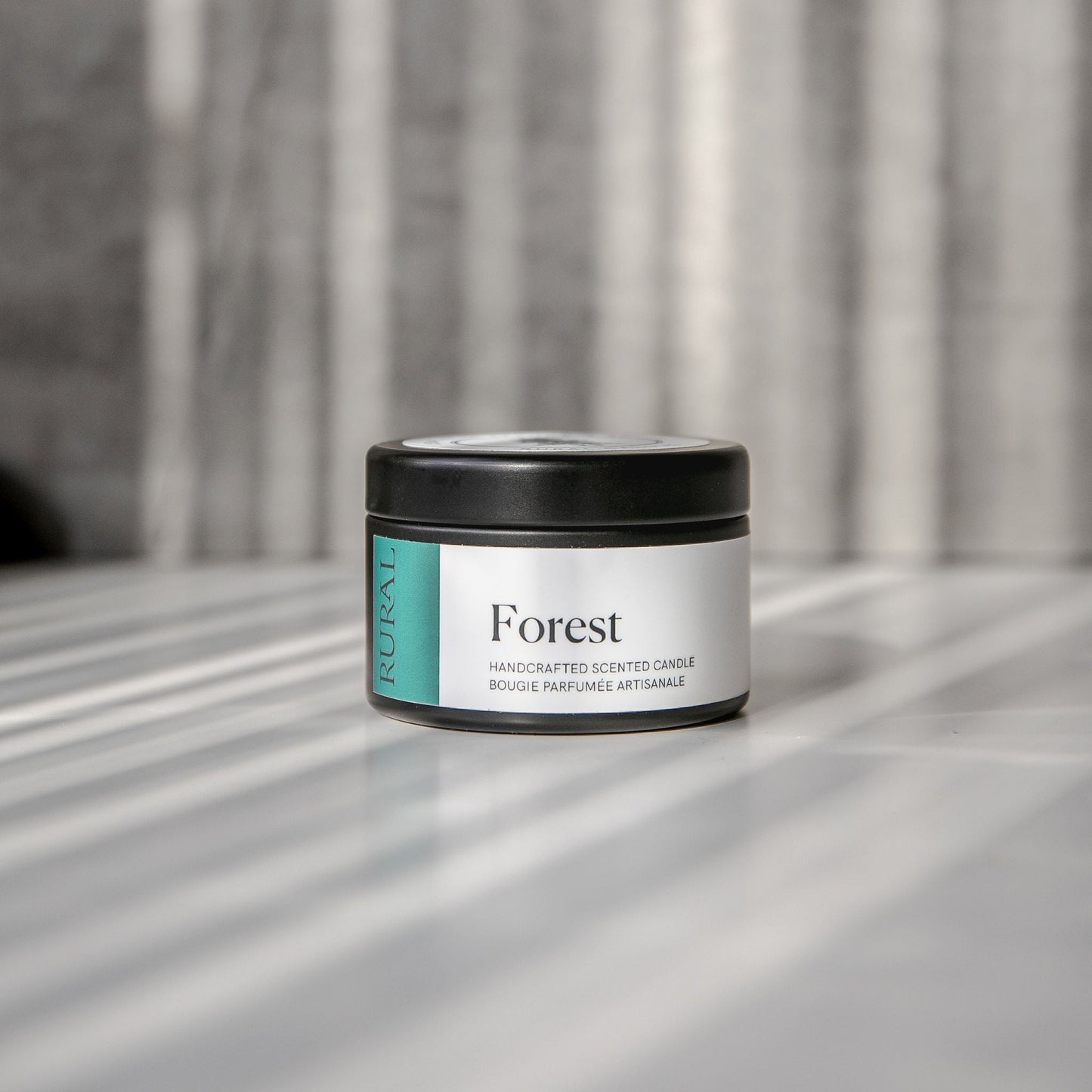 Forest scented black candle tin with green and white label on a reflective surface with a neutral background.