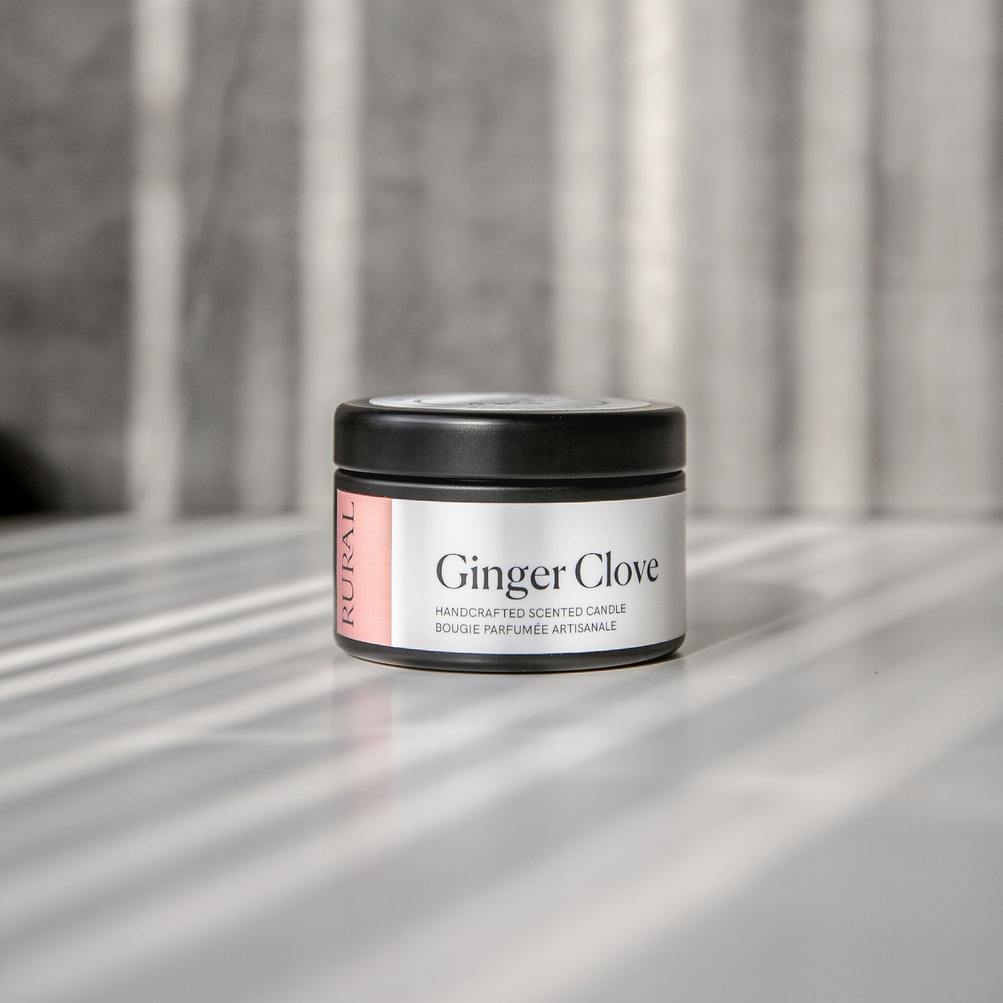 Ginger Clove scented black candle tin with brown and white label on a reflective surface with a neutral background.