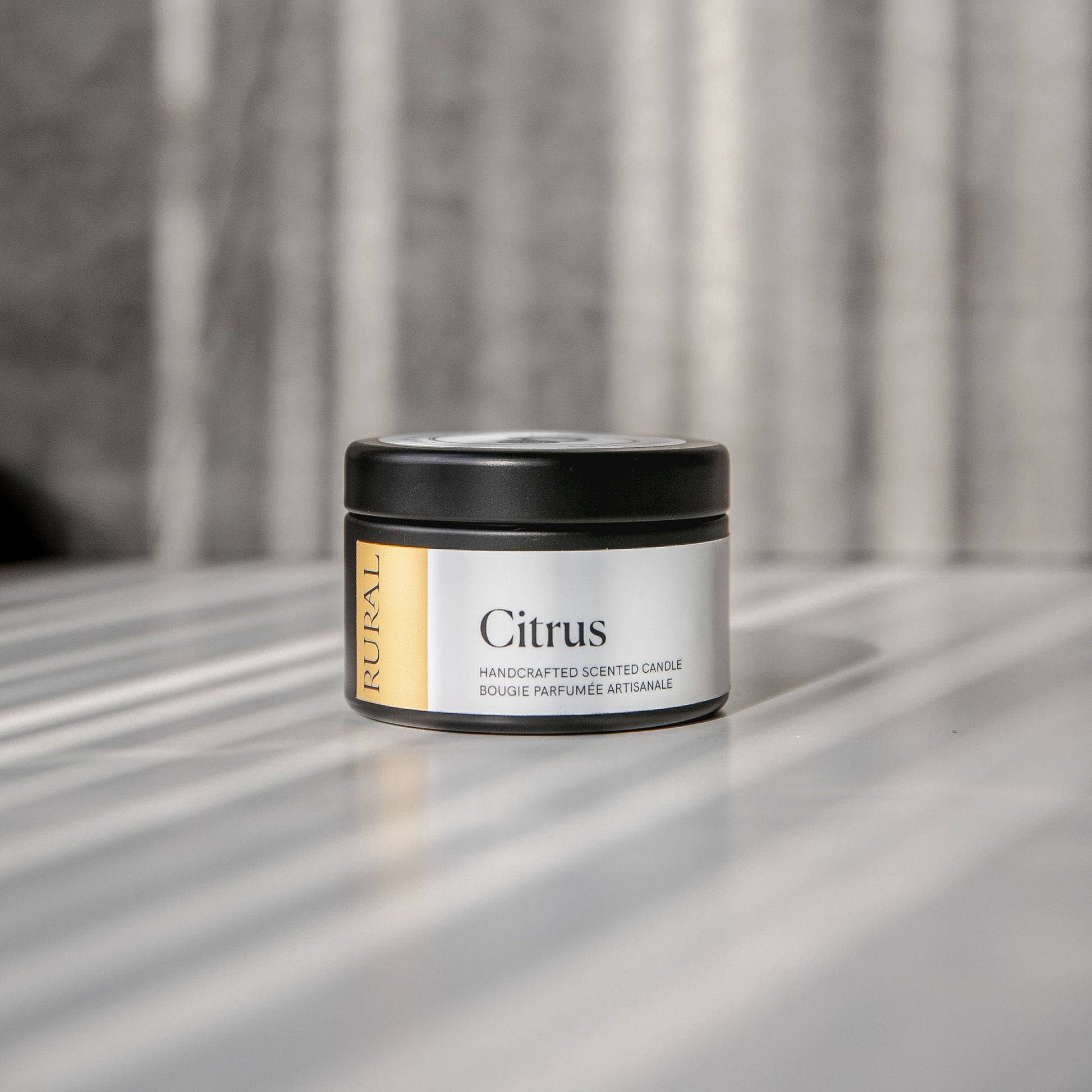 Citrus scented black candle tin with yellow and white label on a reflective surface with a neutral background.