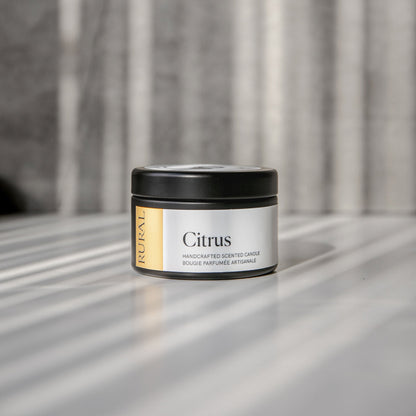 Citrus scented black candle tin with yellow and white label on a reflective surface with a neutral background.