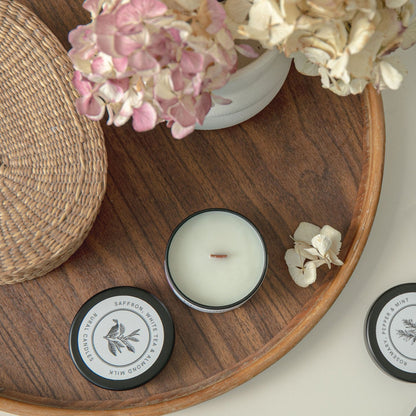 Candles with decorative labels on a wooden tray with flowers and a box of candles.
