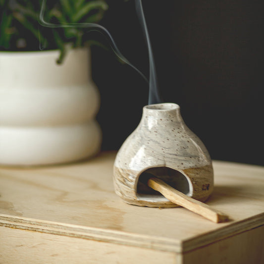Ceramic incense burner with smoke on a wooden surface next to a plant