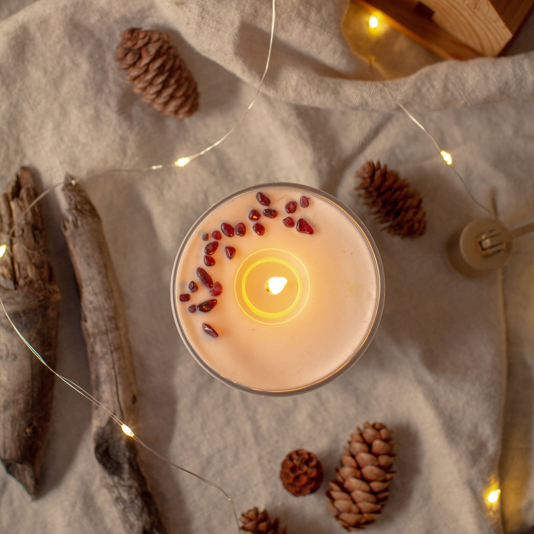 Top view of the RURAL Candles pomegranate candle with a nice flame. We can see the garnet gemstones on the candle. The setting is rustic cottage cozy.