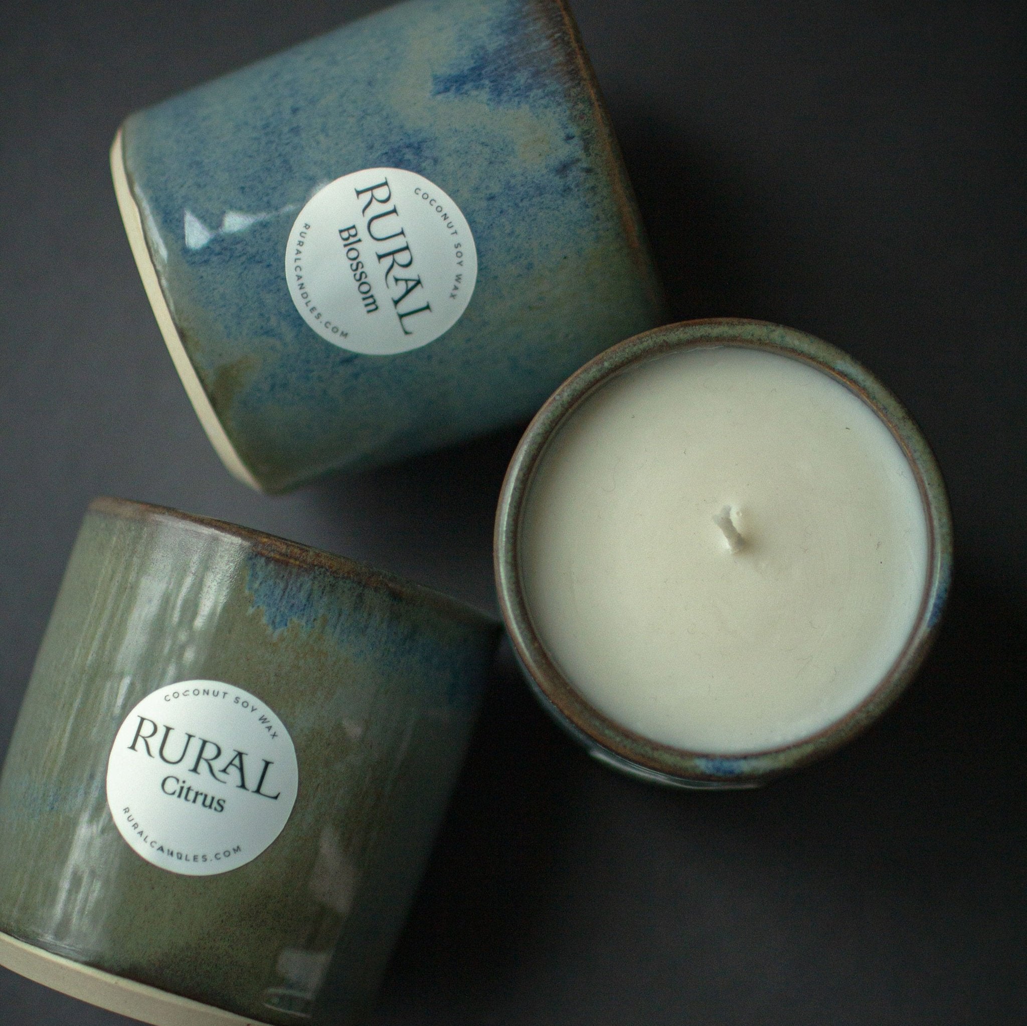 Photo of a group of three handcrafted pottery candles with a beautiful blue green and brown glaze, with white round RURAL Candles labels indicating Blossom and Citrus fragrances.